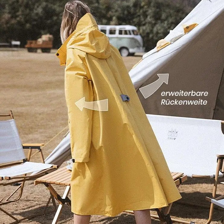 regenmantel damen wasserdicht atmungsaktiv leicht, gelber regenmantel extra lang für Damen getragen von einer blonden schlanken Frau, nach hinten blickend vor einem Camping Platz. Die Rückseite des wasserdichten Parkas gelb sichtbar mit erweiterbarer Rückenweite.
