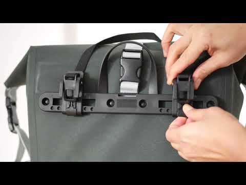 Video zeigt leichte Montage von grüner Fahrradtasche von Bomence am Fahrrad. Zuerst wird Tasche von verschieden Perspektiven gezeigt. Im Anschluss wird Verschluss demonstriert. Frau bringt die Tasche an ihr Fahrrad an und fährt durch die Stadt.