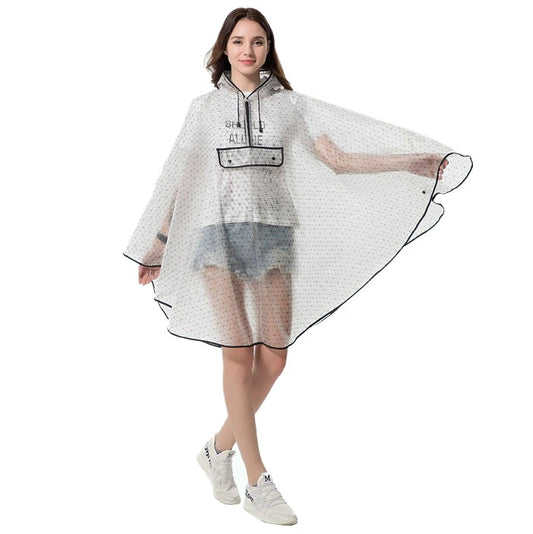 Regenponcho durchsichtig mit Muster, vorne mit Tasche und Kapuze. Frau mit Shorts trägt das Regencape hebt links den Arm hoch und schaut in die Kamera.