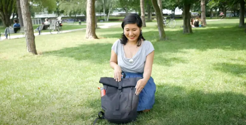 Video vom schwarzen Rolltop Rucksack. Demonstration seiner Funktionen und Taschen durch eine Frau.