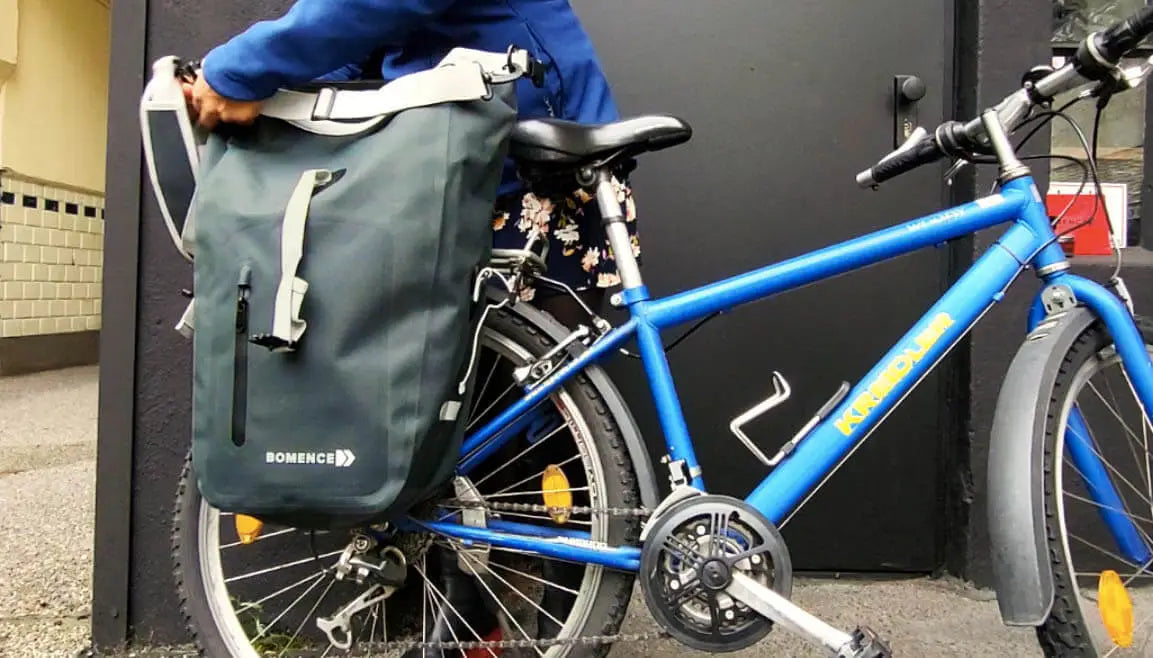 grüne Fahrradtasche Video am Mountainbike. Frau befestigt / montiert die Gepäckträgertasche hinten am Gepäckträger und demontiert sie. Darstellung der Schultergurt draußen vor dunklem Hintergrund in der City.