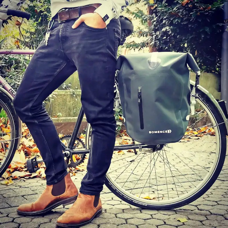 Bild zeigt Mann in Alltagssituation. Herr steht entspannt mit Rad in der Natur. Grüne Fahrradtasche Wasserdicht von Bomence hängt am Gepäckträger.