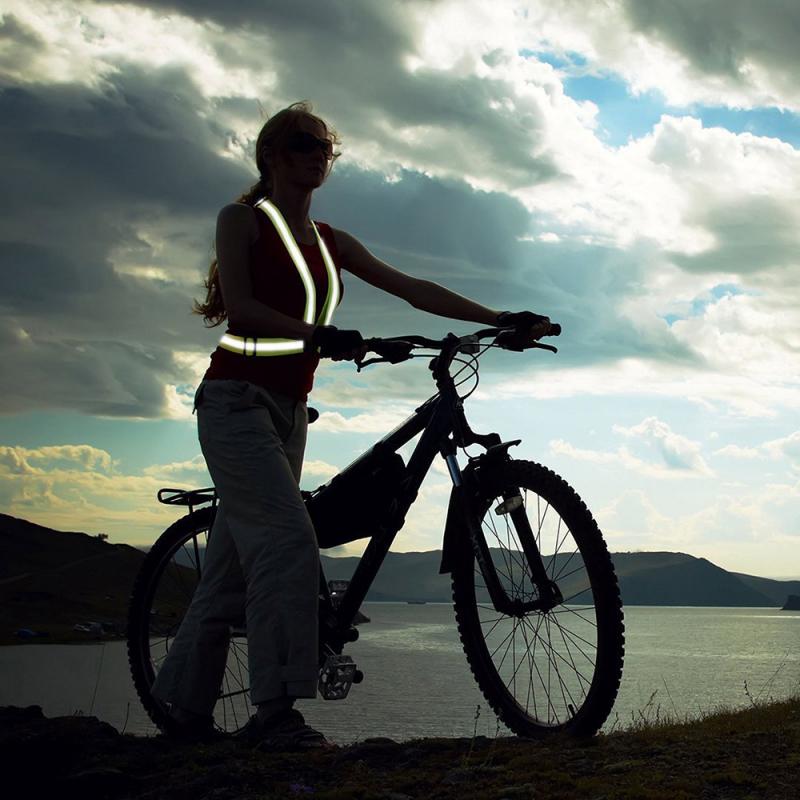 Frau mit Fahrrad und Schutzweste am See bei Abenddämmerung. Reflektoren leuchten.